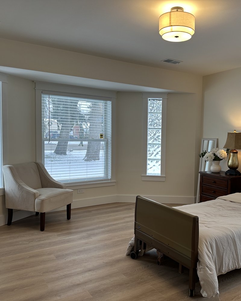 Spacious resident bedroom with a bay window, armchair, and hospital bed